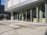 an empty brick road in front of a modern building with large glass windows and doors