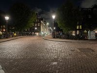 an empty cobblestone street at night with bicycles parked along the curb and buildings in the background