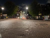 an empty cobblestone street at night with bicycles parked along the curb and buildings in the background