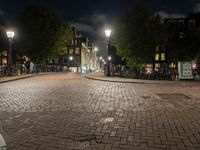 an empty cobblestone street at night with bicycles parked along the curb and buildings in the background