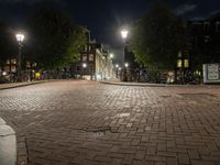 an empty cobblestone street at night with bicycles parked along the curb and buildings in the background