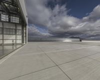 a view of an empty commercial airplane tarmac by the ocean with dramatic clouds behind