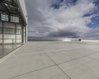 a view of an empty commercial airplane tarmac by the ocean with dramatic clouds behind