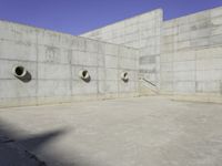 three empty, concrete, round holes in a concrete wall with a blue sky in the background