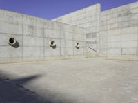 three empty, concrete, round holes in a concrete wall with a blue sky in the background