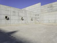 three empty, concrete, round holes in a concrete wall with a blue sky in the background