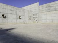 three empty, concrete, round holes in a concrete wall with a blue sky in the background