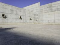 three empty, concrete, round holes in a concrete wall with a blue sky in the background