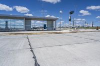 empty concrete lot with empty parking lot with parking spots and poles on the pavement and in the background, with an intersection and clouds