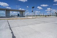 empty concrete lot with empty parking lot with parking spots and poles on the pavement and in the background, with an intersection and clouds