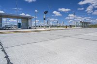 empty concrete lot with empty parking lot with parking spots and poles on the pavement and in the background, with an intersection and clouds