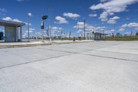 empty concrete lot with empty parking lot with parking spots and poles on the pavement and in the background, with an intersection and clouds