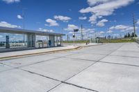 empty concrete lot with empty parking lot with parking spots and poles on the pavement and in the background, with an intersection and clouds