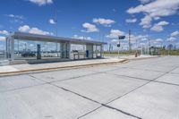 empty concrete lot with empty parking lot with parking spots and poles on the pavement and in the background, with an intersection and clouds