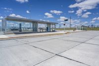 empty concrete lot with empty parking lot with parking spots and poles on the pavement and in the background, with an intersection and clouds