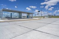 empty concrete lot with empty parking lot with parking spots and poles on the pavement and in the background, with an intersection and clouds