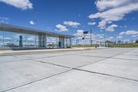 empty concrete lot with empty parking lot with parking spots and poles on the pavement and in the background, with an intersection and clouds