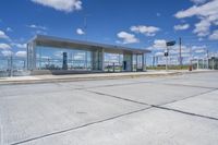 empty concrete lot with empty parking lot with parking spots and poles on the pavement and in the background, with an intersection and clouds