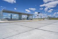 empty concrete lot with empty parking lot with parking spots and poles on the pavement and in the background, with an intersection and clouds