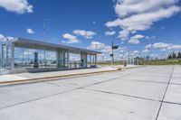 empty concrete lot with empty parking lot with parking spots and poles on the pavement and in the background, with an intersection and clouds