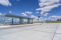 empty concrete lot with empty parking lot with parking spots and poles on the pavement and in the background, with an intersection and clouds