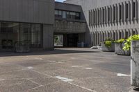 the concrete planters are empty outside of the building, surrounded by flowers and buildings