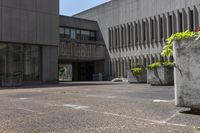 the concrete planters are empty outside of the building, surrounded by flowers and buildings