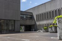 the concrete planters are empty outside of the building, surrounded by flowers and buildings