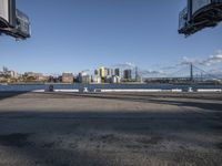 an empty concrete road with a view of city buildings and water in the distance with a few trees around it