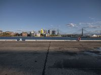 an empty concrete road with a view of city buildings and water in the distance with a few trees around it