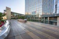 an empty concrete walkway surrounded by tall buildings at sunset with the sky reflecting in the windows