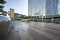 an empty concrete walkway surrounded by tall buildings at sunset with the sky reflecting in the windows