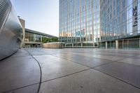 an empty concrete walkway surrounded by tall buildings at sunset with the sky reflecting in the windows