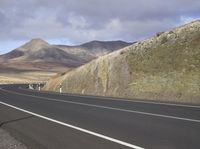 a empty country highway passes through mountains with cloudy skies in the background on a sunny day