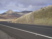 a empty country highway passes through mountains with cloudy skies in the background on a sunny day