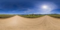 an 360 - view lens view of an empty country road, with the sun shining on the hill side behind