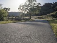 an empty country road with a fence on the side and some grass and trees to the side