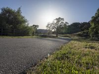 an empty country road with a fence on the side and some grass and trees to the side