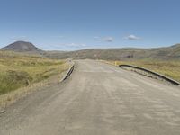 an empty country road crossing over a stream to reach water on the hill and hills in the distance