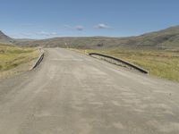 an empty country road crossing over a stream to reach water on the hill and hills in the distance