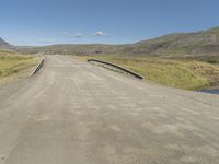 an empty country road crossing over a stream to reach water on the hill and hills in the distance