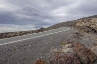 a empty country road in an open desert area near a mountain peak under a cloudy sky