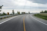 an empty country road in the mountains with the sun shining over the ground and clouds above