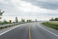 an empty country road in the mountains with the sun shining over the ground and clouds above