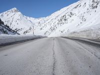 an empty country road winds its way past snow - covered mountains and a blue sky
