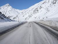 an empty country road winds its way past snow - covered mountains and a blue sky