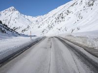 an empty country road winds its way past snow - covered mountains and a blue sky