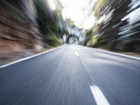 motion blurry photograph of an empty street with trees and rocks in the background and a car driving on a narrow country road