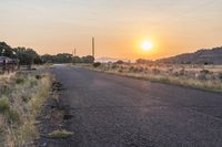 an empty country road with telephone poles at sunset on the other side of it and grass in front of the road