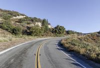 an empty country road on a hillside side surrounded by mountains and grasses is deserted yet it has just passed